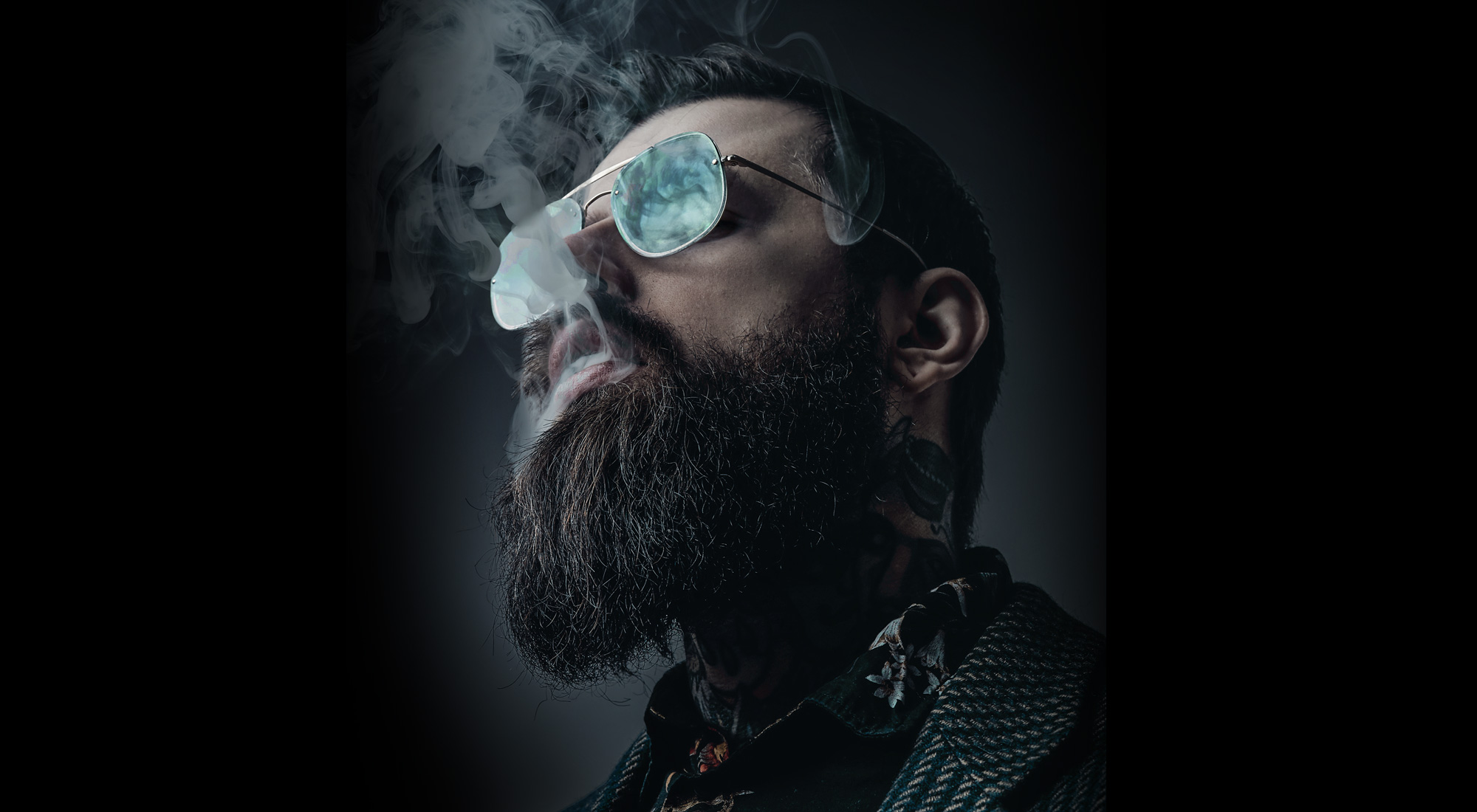 man with glasses blowing smoke